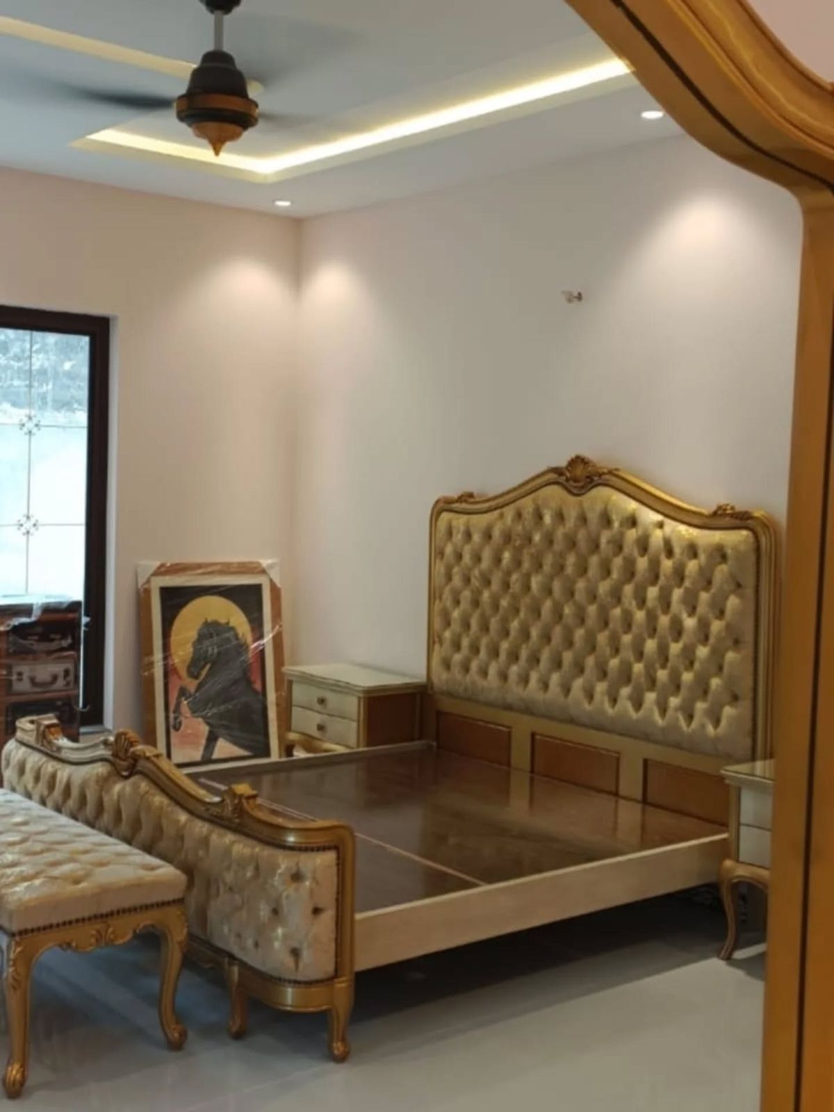 Bed with a carved, gilded tufted headboard and a matching bench in a finished room