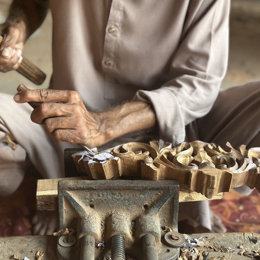 Hands carving an ornamental wooden piece held in a vice